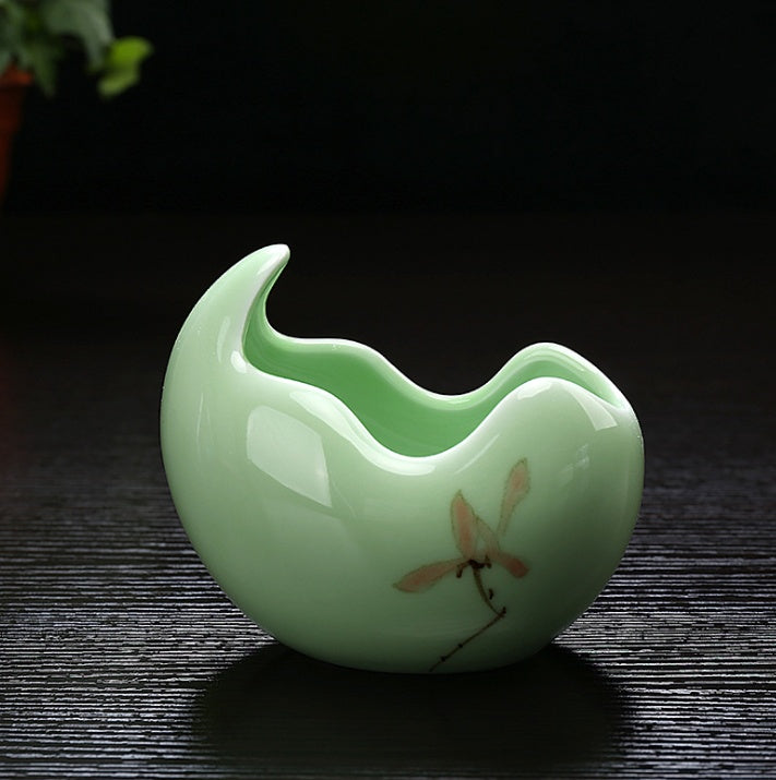 Green ceramic teapot with a dragonfly design on a dark surface