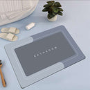 Mat, comforters, gray bathmat with 'Bathroom' text on a light blue surface with slippers and a plant.