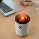 Small cylindrical device with glowing interior on a wooden desk next to a laptop.